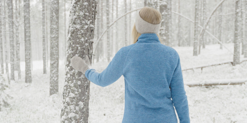 Nainen kävelee metsässä ensilumen aikaan, päällään Ruskovillan taivaansininen villafleecetakki ja lapaset.